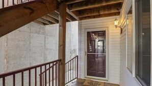Una escalera de madera que conduce a una puerta con un panel de vidrio, un felpudo con un mensaje y un accesorio de iluminación fijado a la pared.
