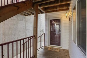Eine Holztreppe führt zu einer Tür mit Glasfenster, einer Fußmatte mit Aufschrift und einer Wandleuchte.