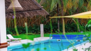 A swimming pool with lounge chairs, a thatched-roof structure, and tropical vegetation.