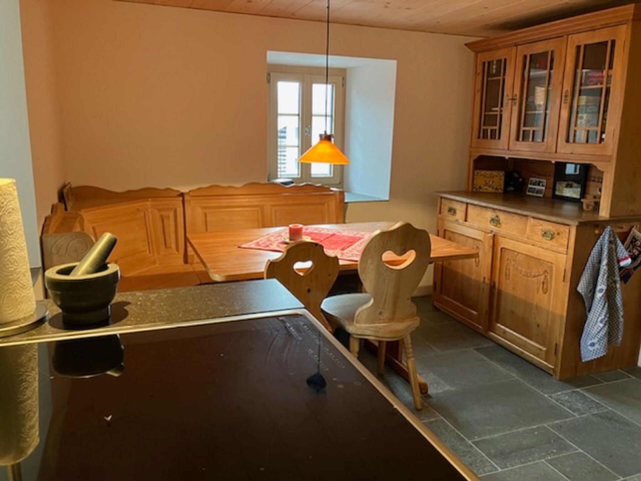 A room with a wooden dining table, a chair, a wooden cabinet, and a window with a lamp.