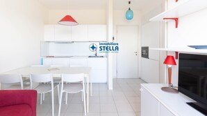Una cocina moderna con armarios blancos, una mesa de comedor con sillas, un sofá rojo y un televisor sobre un mueble blanco.