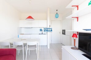 Eine moderne Küche mit weißen Schränken, einem Esstisch mit Stühlen, einem roten Sofa und einem Fernseher auf einem weißen Schrank.