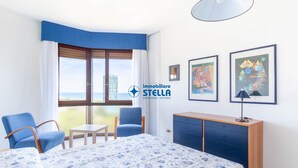 Habitación de hotel con una cama, dos sillas, una mesita, un armario y vista al mar.