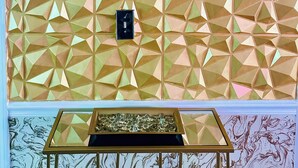 A geometric patterned wall with a small black box and a glass table with a marble-like design.