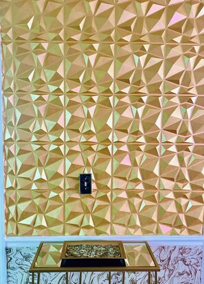 A geometric patterned wall with a small black box and a glass table with a marble-like design.