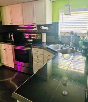 A modern kitchen with stainless steel appliances, a black countertop, and white cabinetry.