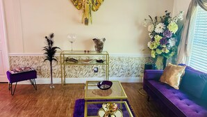 A living room with a purple sofa, a glass coffee table, a decorative elephant wall piece, a floral arrangement, and a marble-patterned wall.