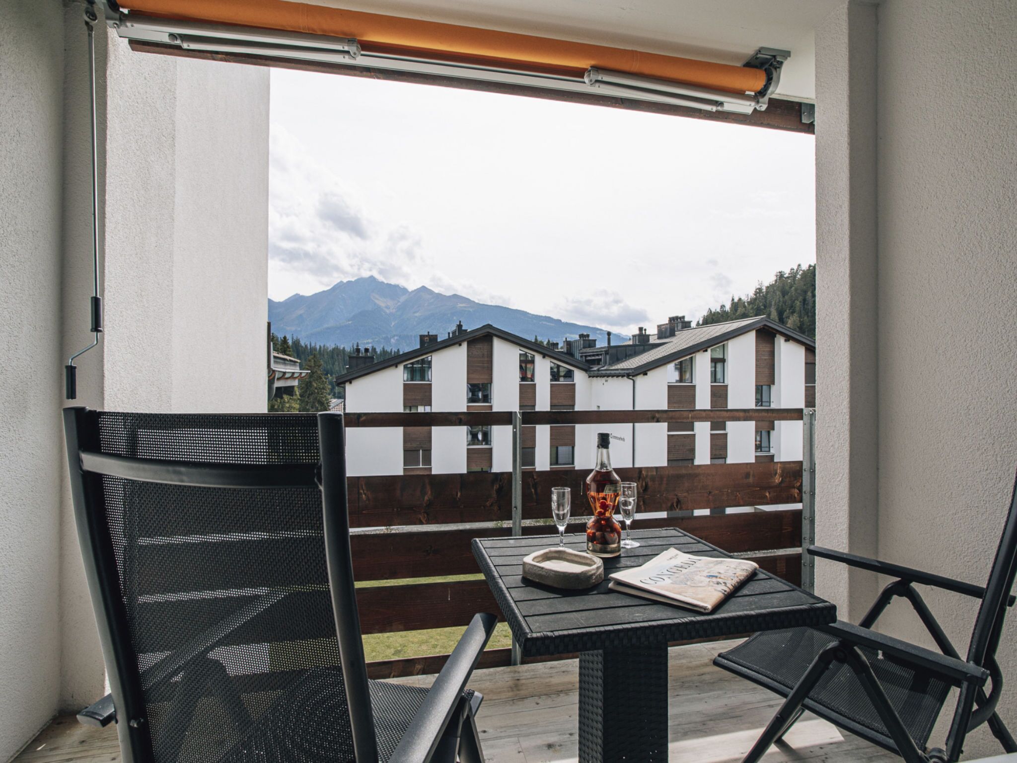 A balcony with a table, chairs, a bottle, glasses, and a magazine.