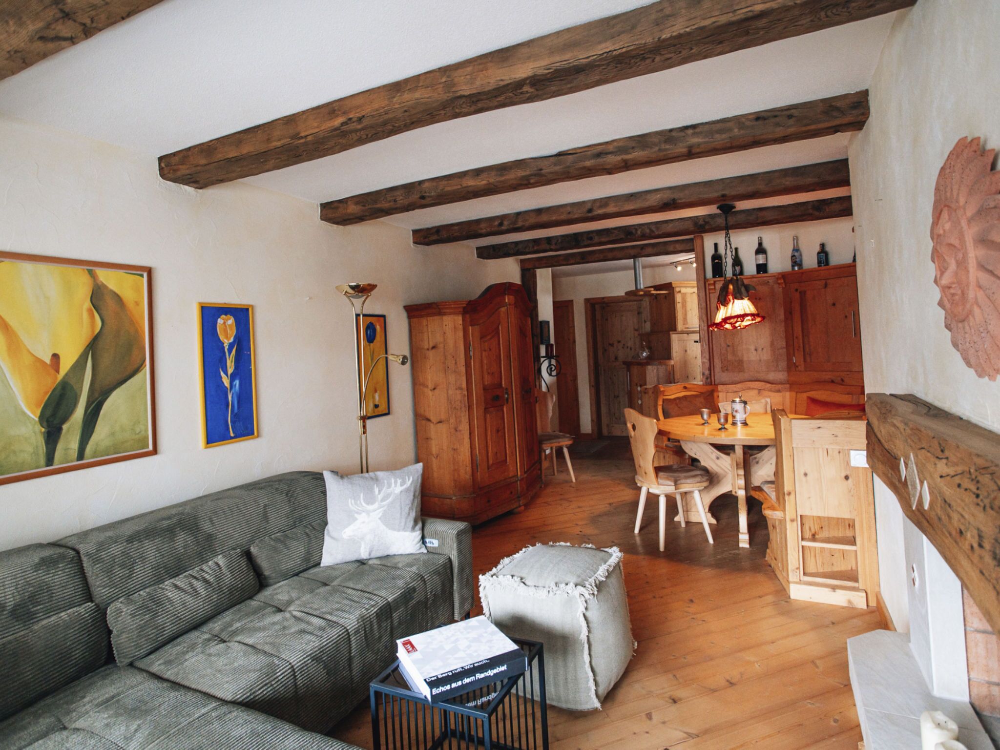 Un salon chaleureux avec un canapé, une petite table sur laquelle repose un livre, et un coin repas en bois avec des chaises.