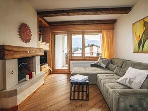 Ein Wohnzimmer mit Kamin, Holzböden, einer Couch und Blick auf Berge durch ein großes Fenster.