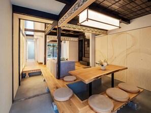A modern interior with a wooden table and benches, a staircase, and a wall with abstract patterns. - Wakaba Machiya House (Kyoto)