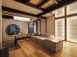 A modern interior with a wooden dining table, a sofa, and a large window with traditional sliding doors. - Wakaba Machiya House (Kyoto)