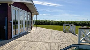 A wooden deck with a white railing, a glass door entrance, and a hedge in the background. - Awesome home in Rødby with WiFi (Rødby)