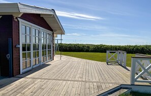 A wooden deck with a white railing, a glass door entrance, and a hedge in the background. - Beautiful home in Rødby with WiFi (Rødby)