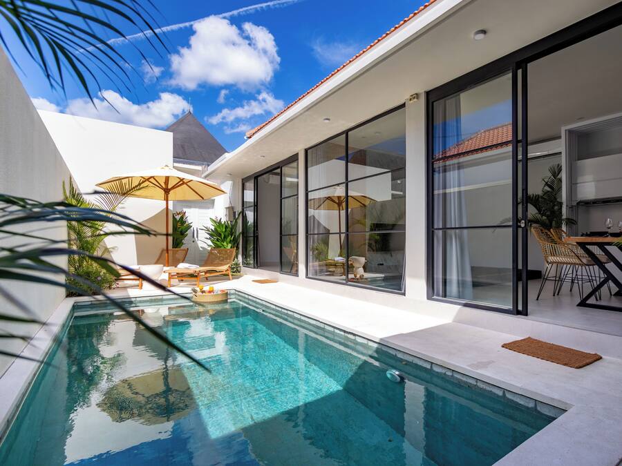 A modern outdoor pool area with a clear blue pool, sun loungers, and a dining area with chairs and a table.