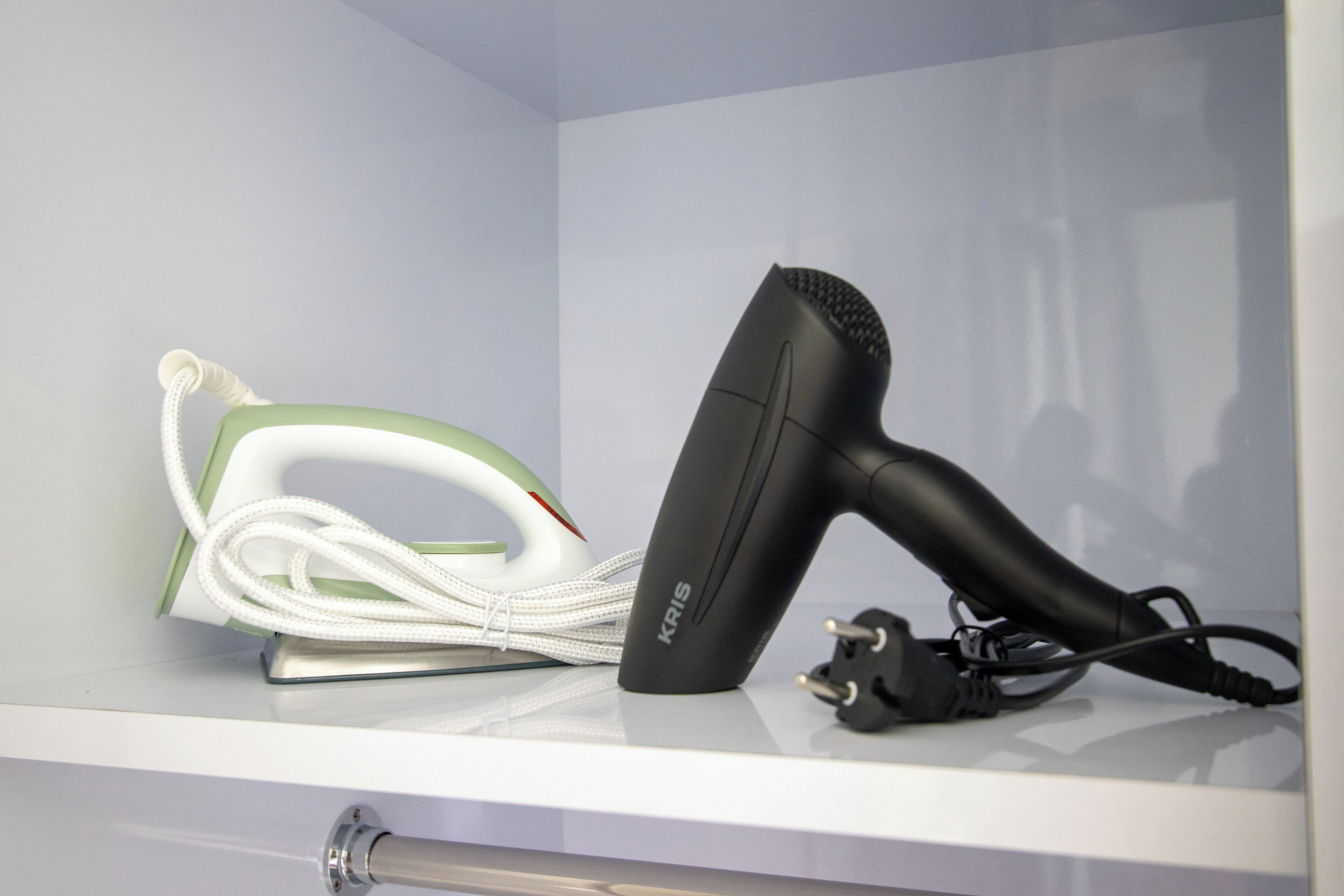 A white shelf with a hair dryer and a green and white iron.