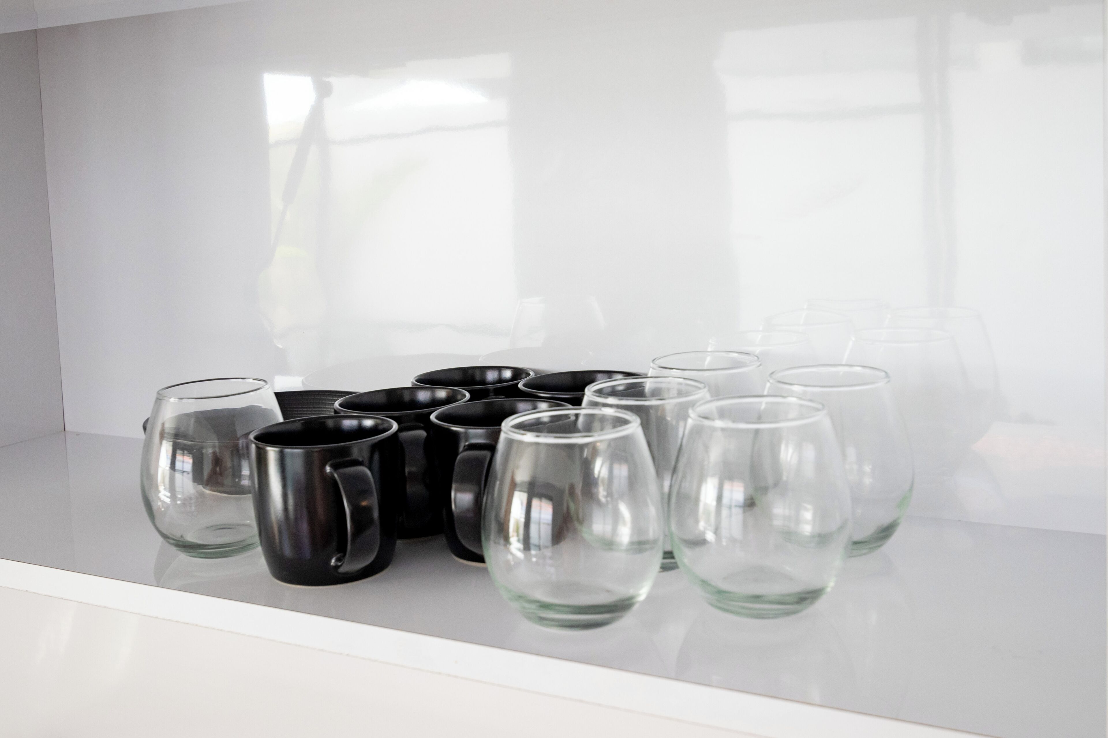 A white shelf with black and clear glass mugs and a clear glass.