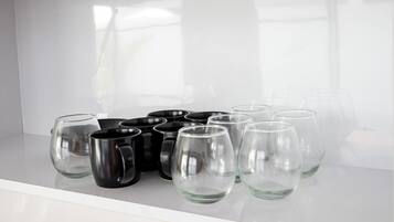 A white shelf with black and clear glass mugs and a clear glass.