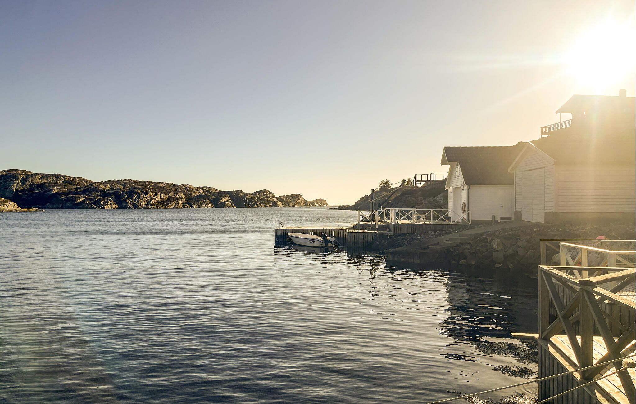 Un paysage côtier avec un quai, un petit bateau et un bâtiment dont l’entrée donne sur le quai.