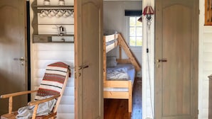 Ein Zimmer mit einem Etagenbett, einem Holzhocker und einem Regal mit Küchenutensilien.