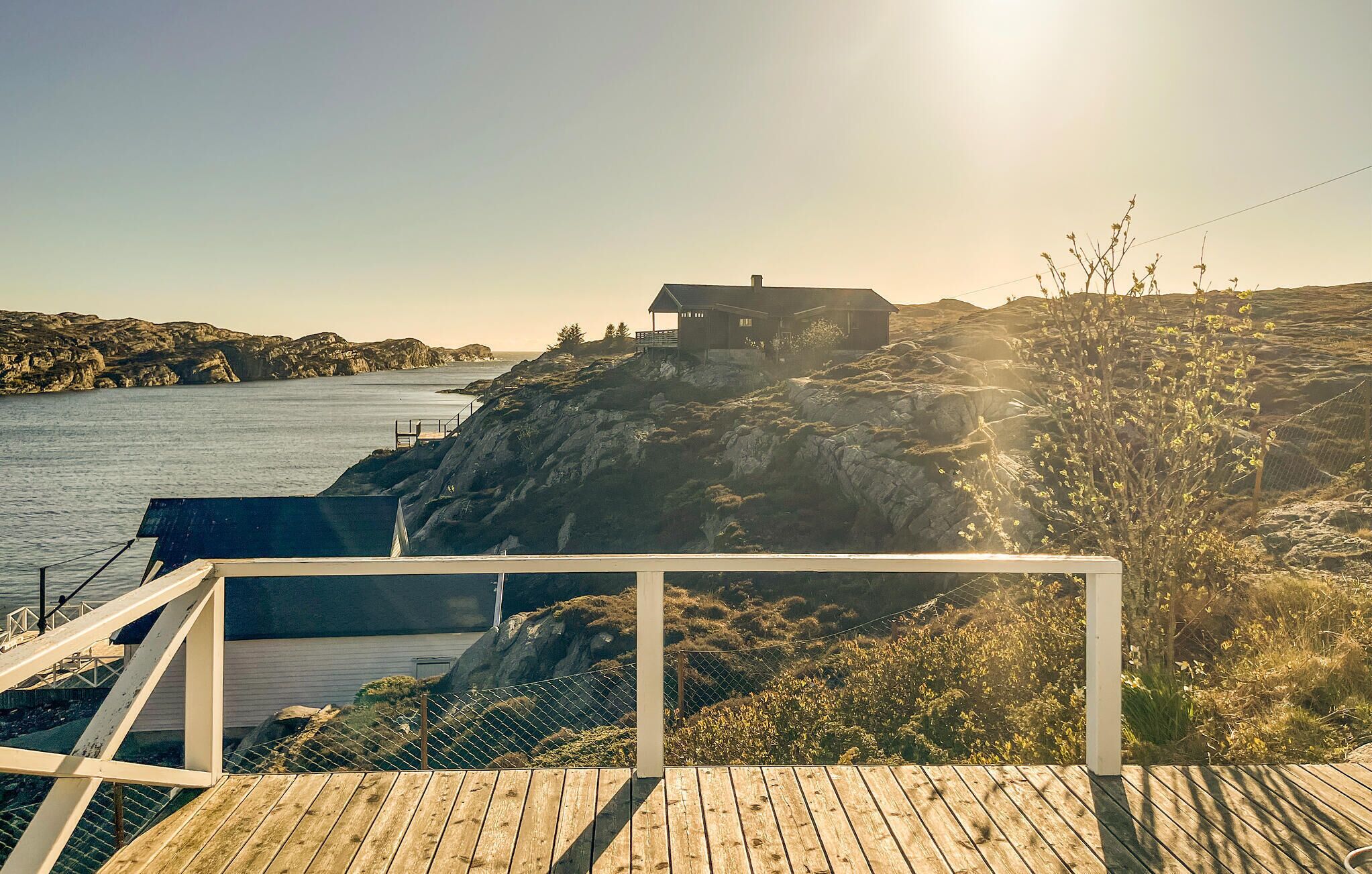 En fastighet vid kusten med en träveranda, ett hus som ligger på en klippa med utsikt över havet och ett bergigt landskap.