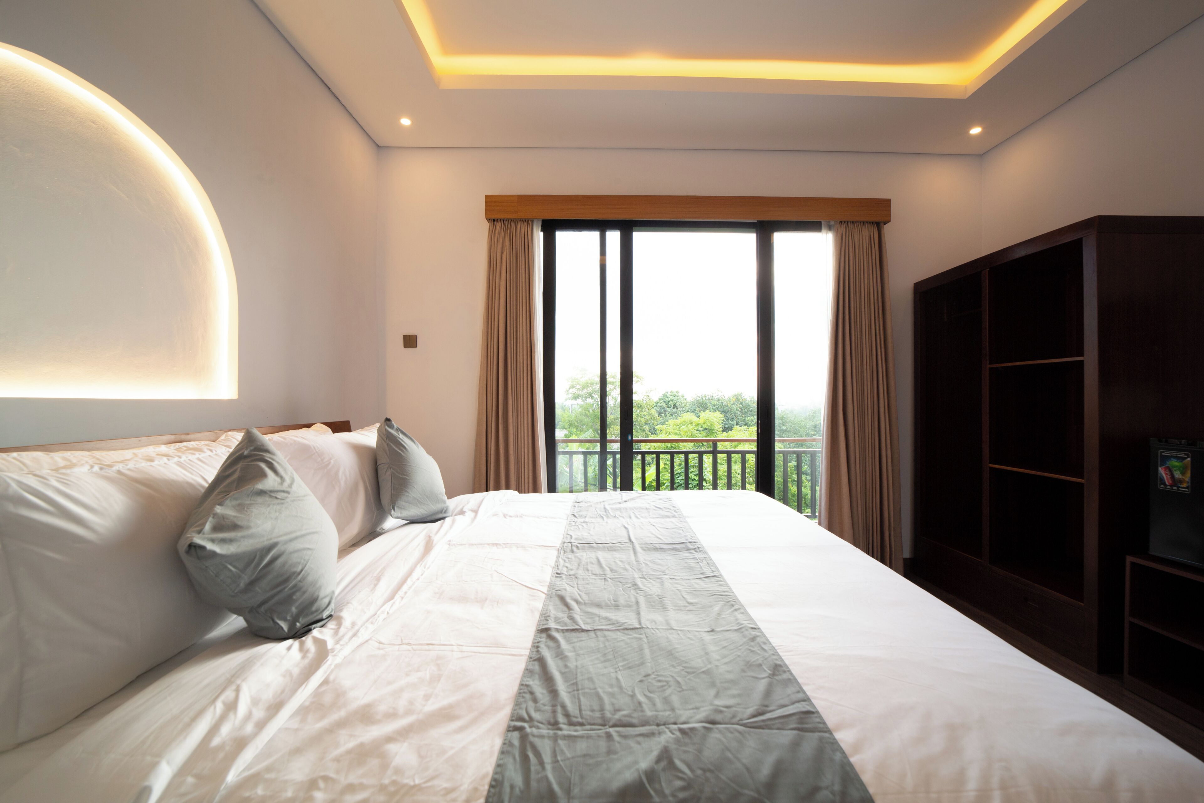 A hotel room with a large bed, a wardrobe, a window with curtains, and a balcony.