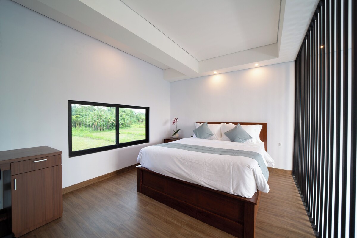 Un dormitorio con un ventanal grande, una cama de madera, una mesita de noche y un armario.