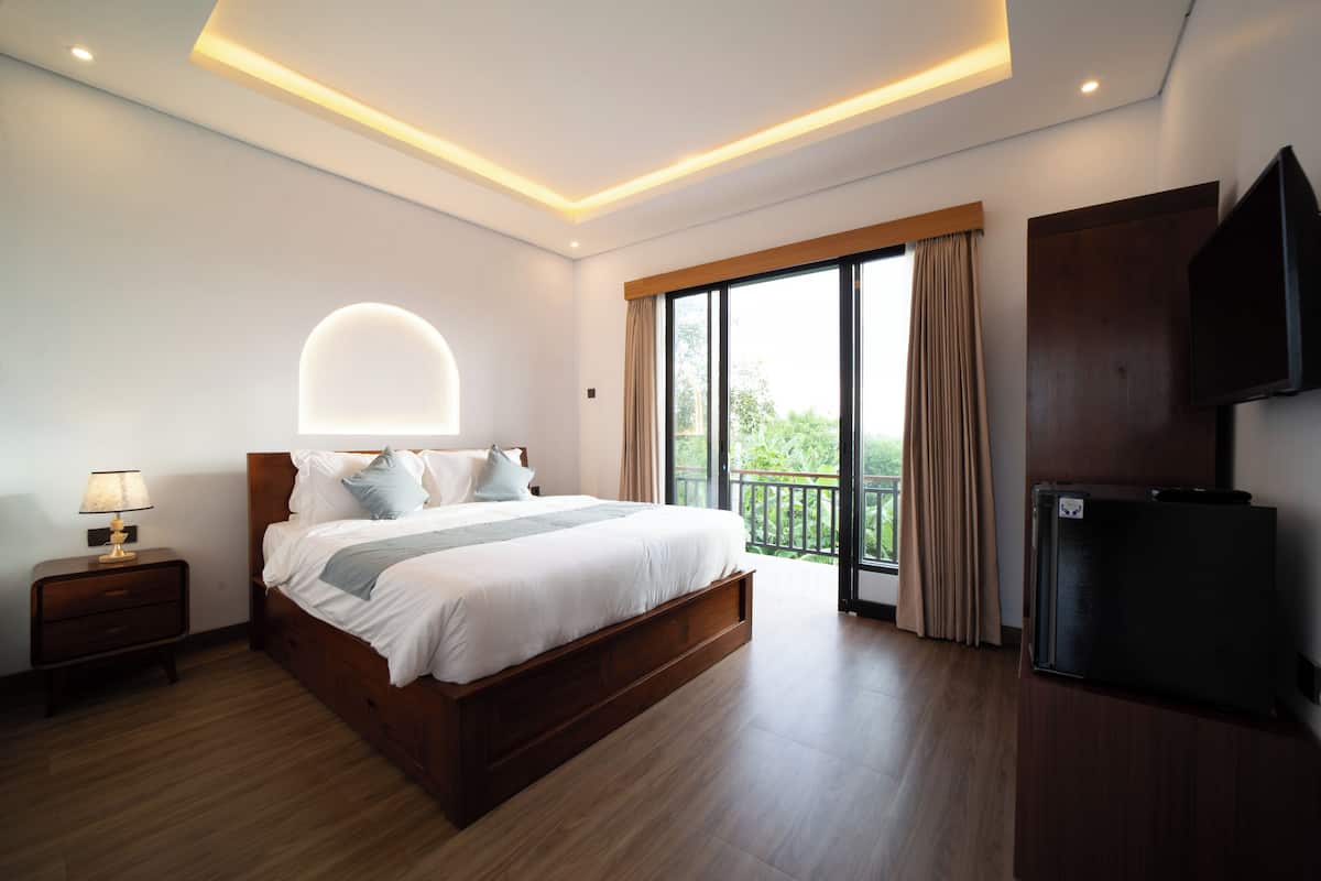 A modern hotel room with a large bed, a flat-screen TV, a nightstand, and a balcony with curtains.