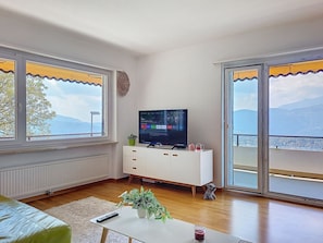 Ein Wohnzimmer mit Fernseher, Pflanze, Fernbedienung und einem Getränk auf einem Tisch.