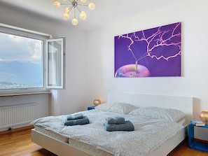 Ein Schlafzimmer mit Bett, einem Fenster mit Aussicht, einem Wandbild und einer Deckenleuchte.
