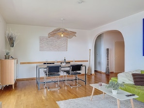 Ein modernes Wohnzimmer mit Essbereich, Holzböden, einem grünen Sofa, einem weißen Couchtisch und einer hängenden Deckenleuchte.