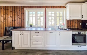 A kitchen with white cabinets, a double sink, a stove, and a window with a view of trees.