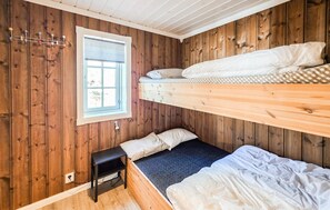 A room with wooden walls, a window with a geometric pattern, a bunk bed, a small table, and a carpeted floor.