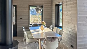 A modern dining room with a long table, six chairs, a vase with flowers, and a large window with a view of a building. - Awesome home in Tjørhom with sauna (Tjørhom)