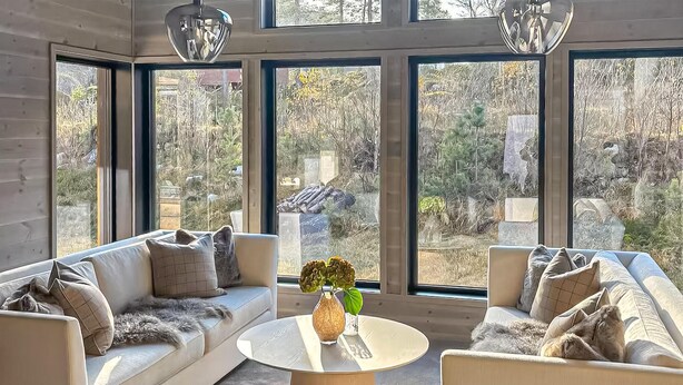 A modern living room with a sofa, armchairs, a coffee table, and large windows offering a view of a garden. - Awesome home in Tjørhom with sauna (Tjørhom)