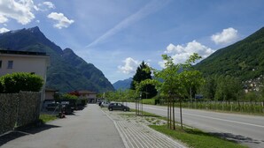 Une route asphaltée bordée de voitures garées, un bâtiment avec un toit rouge et des montagnes en arrière-plan.