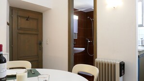 Une pièce comprenant une table à manger, des chaises, une bouteille de vin, des verres, une bougie, ainsi qu’un espace douche avec un lavabo et un radiateur.