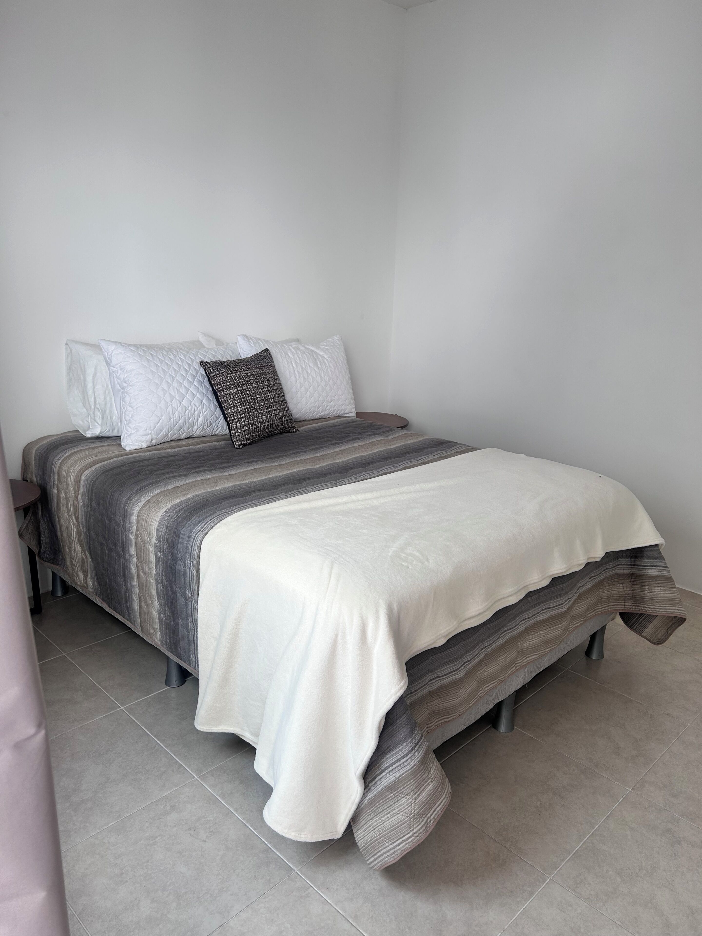 A bed with a grey and white striped bedspread, a white quilted pillow, and a patterned pillow.