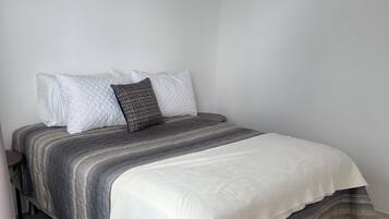 A bed with a grey and white striped bedspread, a white quilted pillow, and a patterned pillow.