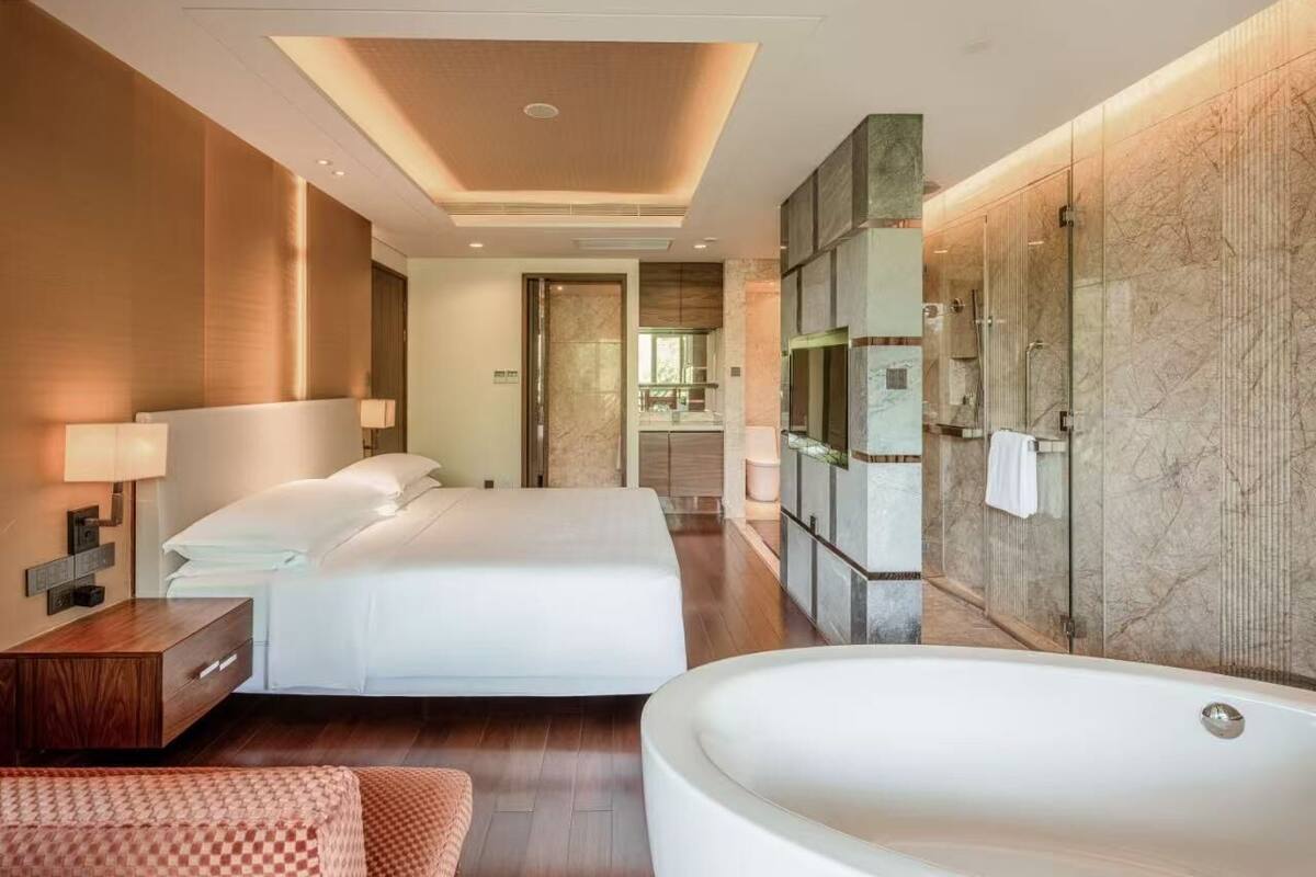 Habitación de hotel con dos camas, una bañera grande, un tocador con espejo y cabina de ducha.
