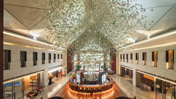 A spacious lobby with a central bar area, seating arrangements, and a ceiling adorned with hanging plants. - TAI LAKE DREAMLOHAS VILLA RESORT (Suzhou)