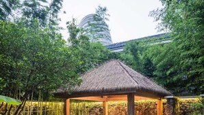 A gazebo with a thatched roof, stone walls, and a circular seating area in a garden setting. - TAI LAKE DREAMLOHAS VILLA RESORT (Suzhou)