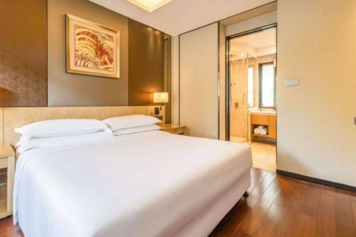 Habitación de hotel con una cama grande, una mesita de noche, una lámpara fijada a la pared y una puerta que da a un baño.