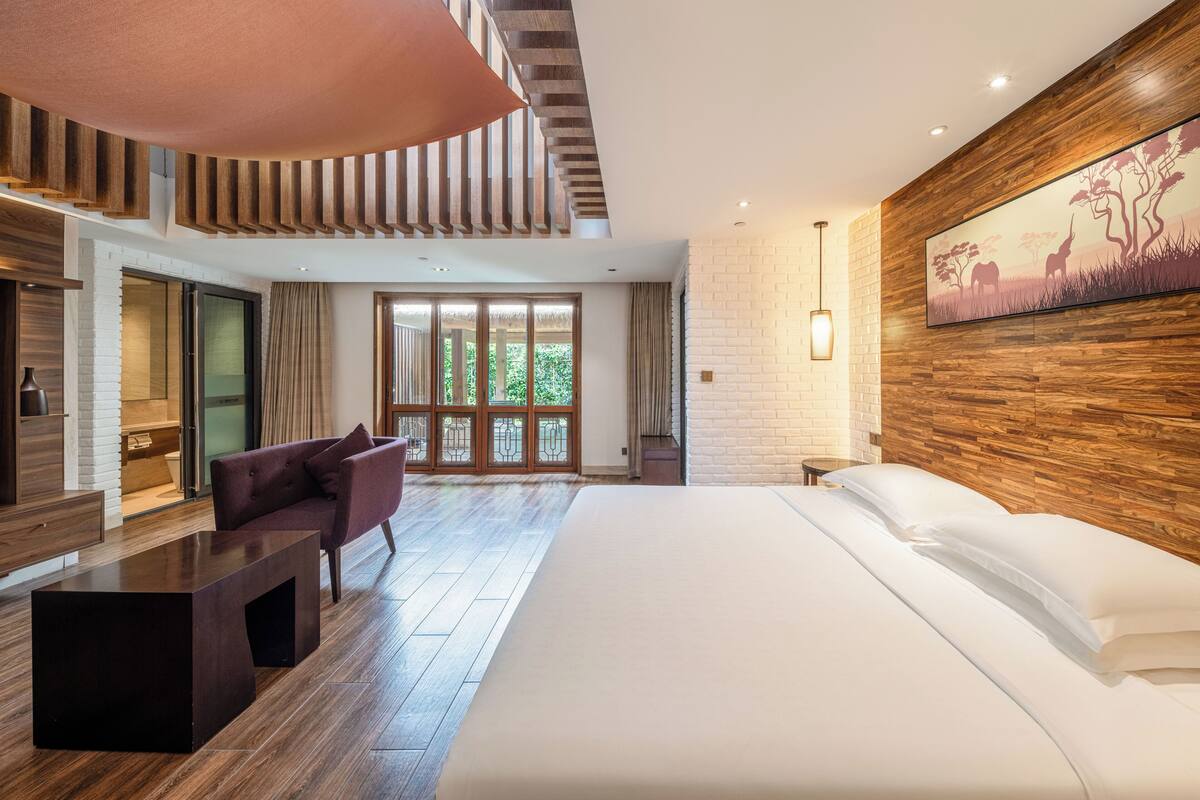 Una habitación de hotel moderna con una cama grande, un área de descanso, una mesa de comedor y un ventanal con vistas.