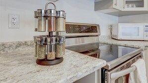 A kitchen with a stainless steel range hood, a microwave, and a marble countertop.
