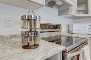A kitchen with a stainless steel range hood, a microwave, and a marble countertop.