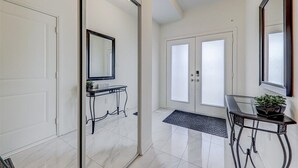 A hallway with a sliding glass door, a black console table with a mirror, a potted plant, and a black mat at the entrance.