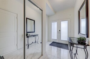 A hallway with a sliding glass door, a black console table with a mirror, a potted plant, and a black mat at the entrance.