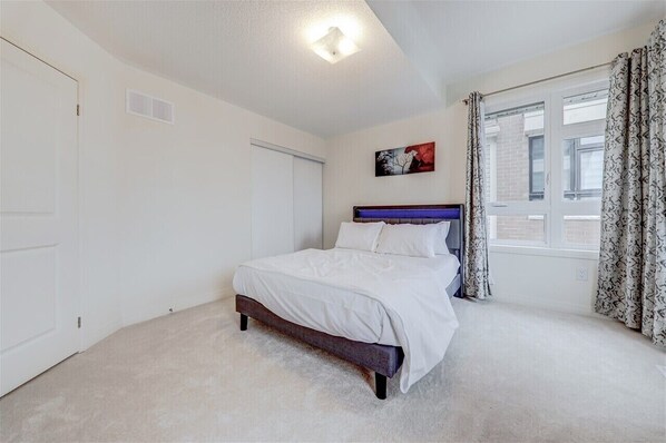 A bedroom with a bed, a window with curtains, a door, and a ceiling light.