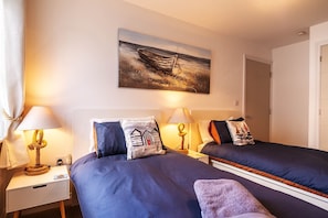 A hotel room with two beds, a painting of a boat on the wall, and a lamp on each nightstand.
